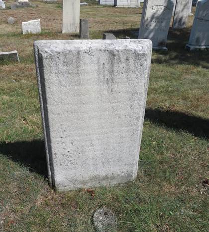 Rectangular marble grave marker with a finished beveled edge. It is weathered with black lichen, and the inscription is almost illegible. A concrete plot marker is set in front, and it is set amid a patchy brown and green grassy area with other grave markers.