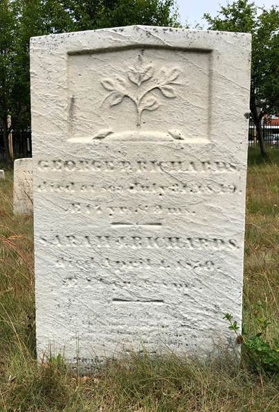 White rectangular marble grave marker with a slight point at the top. A floral motif is inset in a rectangle carved out at the top with an inscription for the Richards below it.