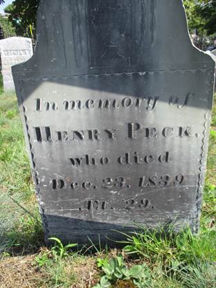 Slate grave marker detail of the inscription for Henry Peck, set in a grass and dirt area with a white grave marker in the background