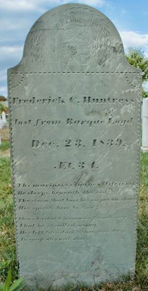 Slate grave marker with a rounded top. An urn and willow design and a long inscription for Fredrick Huntress is carved into it.