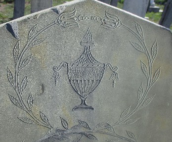 detail of old slate gravestone carved with an urn surrounded with a thin floral garland