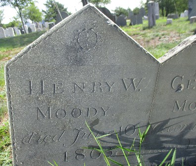 detail of an old slate gravestone carved with a small rosette and Henry W. Moody