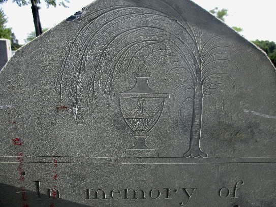 detail of an old slate gravestone carved with a weeping willow over an urn and In memory of