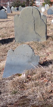 surrounded by the brown turf Eastern Cemetery, the back of an old slate head stone with the front of its foot stone in the foreground