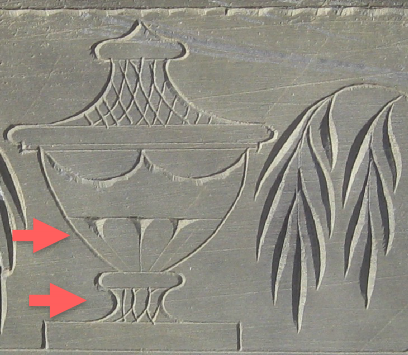 Detail of a slate grave stone with a carving of an urn. Two red arrows point to the flutes and the stem